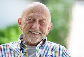 A smiling senior man set against a blurred natural background