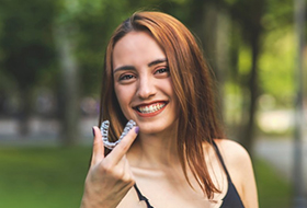 a woman smiling while holding an Invisalign tray