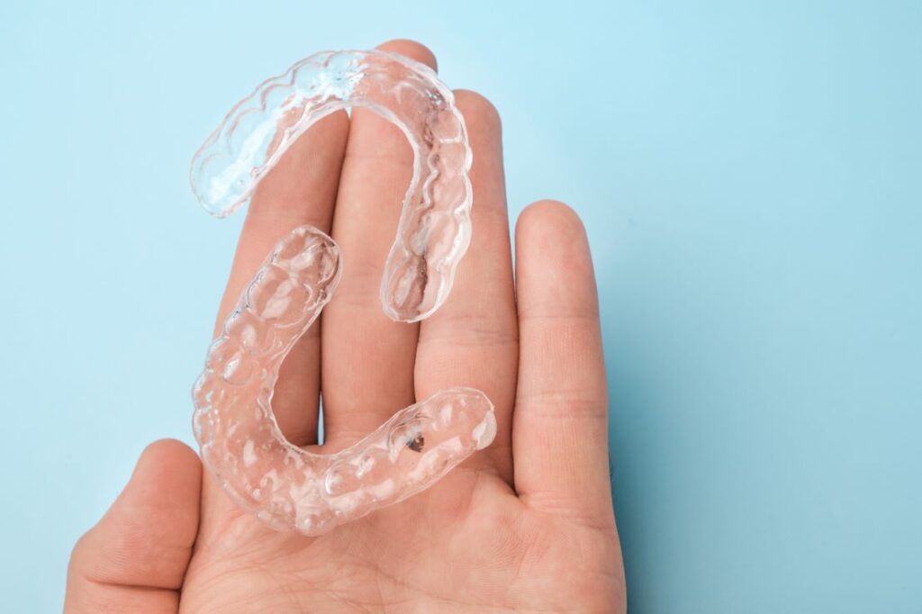 A hand holding a pair of Invisalign aligners.