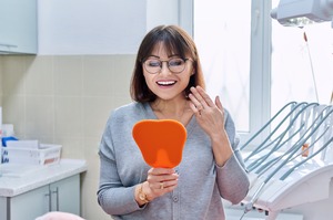 Woman checking smile in mirror while sitting in dental chair